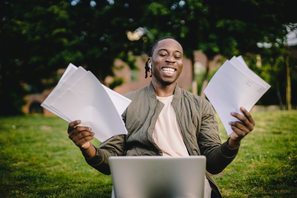 happy young man holding papers with laptop on lap